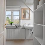 Badezimmer mit Waschbecken, Spiegel und Fenster. Regal und Heizung sind sichtbar.