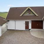 Haus mit braunem Dach, roter Tür und Garage. Grünfelder im Hintergrund.