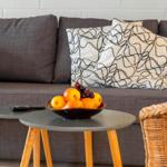 Ein grauer Sofa mit Kissen, ein runder Tisch und Obstschale.