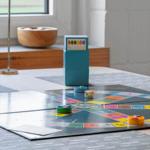 Spielplatte mit Würfeln und Spielsteinen auf Tisch. Fenster mit Blick auf Grünfläche.