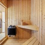 Sauna with wooden walls, bench, and heater. Entrance to bathroom.