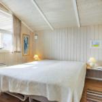 Bedroom with bed, window, and wooden wall. A bedside lamp is next to the bed.