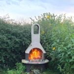 Outdoor stone oven with burning fire in green areas with yellow flowers.