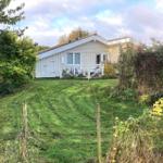 A house with a white fence and green lawn in front of a wooded area.
