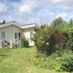A small house with a terrace, surrounded by grass and bushes under a cloudy sky.