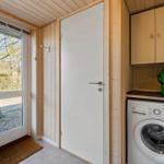 Entrance area with washing machine, wooden walls, and window view of a tree.