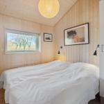 Bedroom with wooden walls, bed, and window overlooking trees.