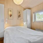 Bedroom with wooden walls, white bed, and window with view of trees.