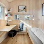 A bedroom with bed, desk, and chair. Wooden walls and windows.