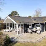 Black house with wooden terrace, sun loungers, and table with chairs.