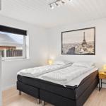 Schlafzimmer mit Bett, Nachttisch und Fenster mit Blick auf Dächer.