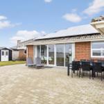 Terrasse mit Tisch, Stühlen und Liegestühlen. Glasfront zum Innenraum. Solarpaneelen auf Dach.