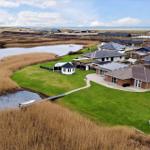Haus mit Garten und Bootssteg am Wasser, Blick auf Strand und Himmel.