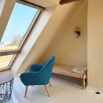 Dachgeschosszimmer mit blauem Sessel, Holzboden und großem Dachfenster.
