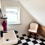 Badezimmer mit schwarz-weißem Fliesenboden, Waschbecken, Stuhl und Fenster.