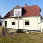 Ein Haus mit rotem Dach und weißer Fassade. Auf dem Dach befindet sich eine Terrasse mit Glasfronten.