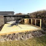 Holzterrasse mit Liegestuhl und Geländer im Freien.