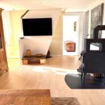 Wohnzimmer mit Holzboden, Kaminofen und Wandfernseher.