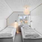Zwei Betten in einem schrägen Dachzimmer mit Fenster und Lampe.