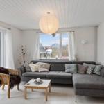 Ein Wohnzimmer mit grauem Sofa, Holztisch und Fenstern mit Blick nach draußen.