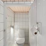 Badezimmer mit Toilette und Dusche, weiße Fliesen und Holzdecke