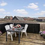 Terrasse mit Tisch, Stühlen und Blumen. Blick auf Häuser und Himmel.