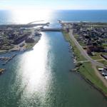 Aerial view of a coastal village with harbor, boats, and surrounding green areas.