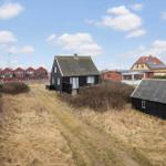 Schwarzes Haus mit Dach und Fenstern, umgeben von Gras und weiteren Gebäuden.