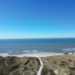 Wanderweg führt von Dünen zu Strand und Meer unter klarem Himmel.