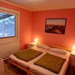 Zimmer mit Doppelbett, Fenster und Kinderbett. Wandfarbe rot. Beleuchtung durch Nachttische.