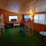 Räumlichkeiten mit Spielplatz, Tisch und Stühlen, grüner Boden, Holzwände und Fenster mit Schneeansicht.