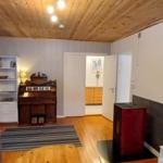 Wohnraum mit Holzboden, Kaminofen und TV. Durchgang zu Schlafzimmer und Küche.