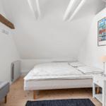 Bedroom with sloped ceiling, white mattress, and wooden floor.