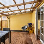 Deck with wooden roof, table, chairs, and grill. Glass door leads to the apartment.