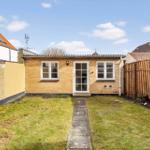 A small house with yellow brick, white door and windows. Yard with lawn and stone path.
