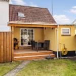 Backyard with terrace, table, chairs, and grill. Yellow extension with roof and window.