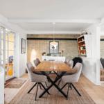 Dining room with wooden table, chairs, and living area in background.