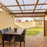 Terrace with table, chairs, and cover. Backyard with lawn and wall.