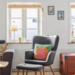 A gray chair with a cushion stands by a window. Next to it is a sofa and a trunk.