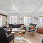 Living room with sofa, two chairs, wooden table, and windows.