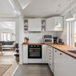 Kitchen with white cabinets and wooden countertop. Living room with sofa in background.