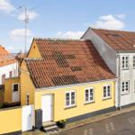 Yellow house with red roof and white windows on a street.