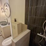 Bad mit Dusche, Waschbecken und Toilette. Schwarze Fliesen und moderne Beleuchtung.