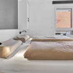 Zwei Betten mit hellen Bettwäsche, Fenster mit Dachziegeln und Schrank an der Wand.