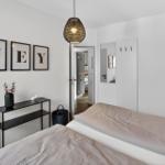 Schlafzimmer mit Bett, Wandbildern und Deckenleuchte. Blick in angrenzenden Raum.