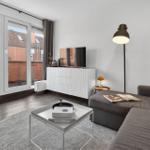 Wohnzimmer mit Sofa, Couchtisch und TV. Durchgang zu Balkon mit Sitzgelegenheit.