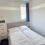Schlafzimmer mit Doppelbett, Nachttisch, Schrank und Fenster mit blauen Vorhängen.