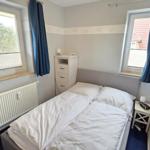 Schlafzimmer mit Doppelbett, zwei Fenstern und Schrank.
