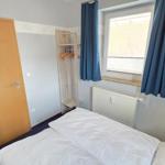 Schlafzimmer mit Bett, Kleiderständer und Fenster mit blauen Vorhängen.