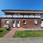 Zweistöckiges Haus mit Balkon, weißen Türen und gepflastertem Hof.